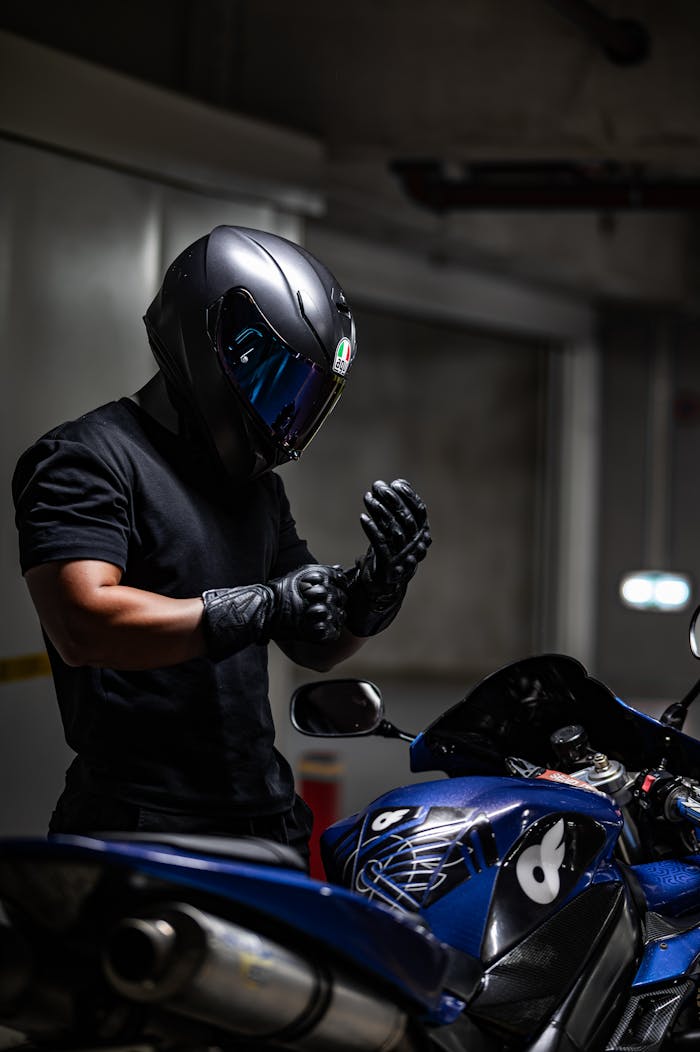 A motorcyclist in a helmet and gloves prepares to ride a blue motorcycle in a dimly lit garage.
